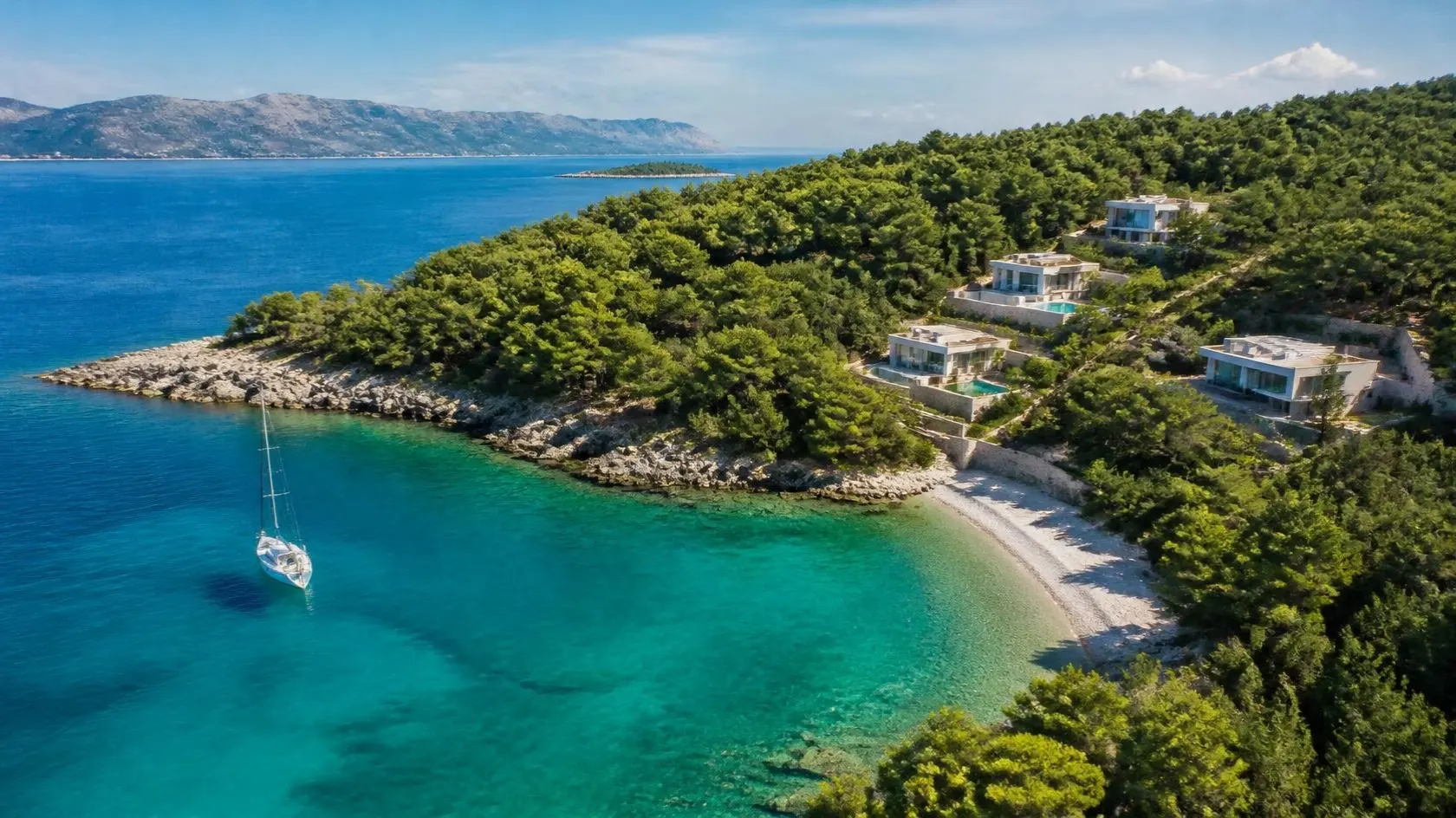 Luftbild einer türkisfarbenen Inselbucht mit Pinienwald, Kiesstrand und Villen am Hang