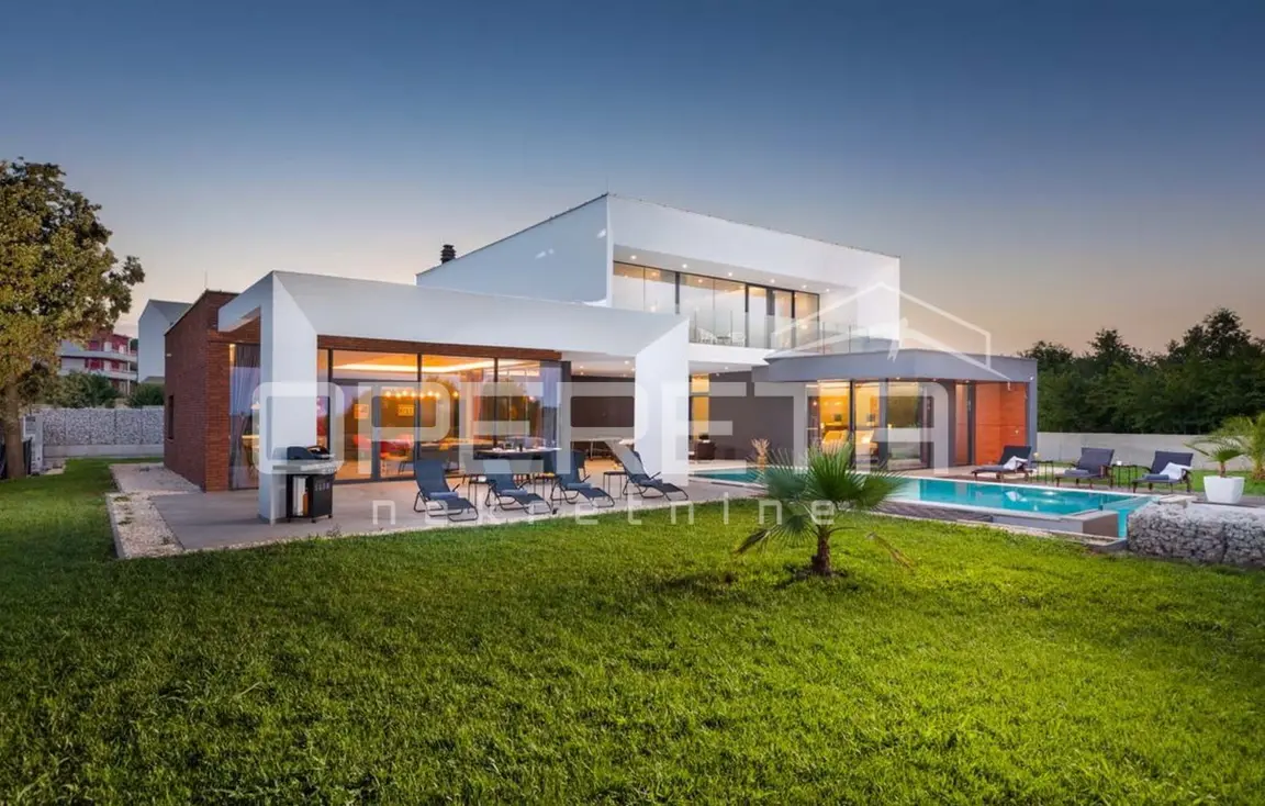 Moderne weiße Villa mit beleuchtetem Pool und Rasen in der Abenddämmerung